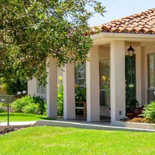 A charming house with a well-maintained lawn and lush greenery surrounding the porch on a sunny day.