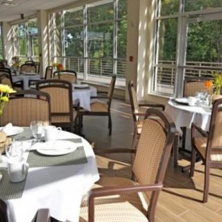 A sunlit dining area with neatly arranged tables and chairs near large windows.