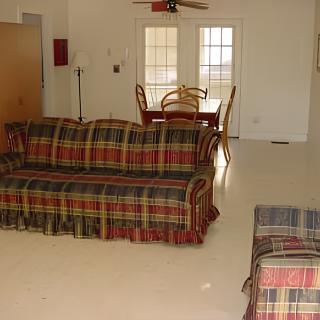 A living room with plaid-patterned sofas and a dining area in the background.