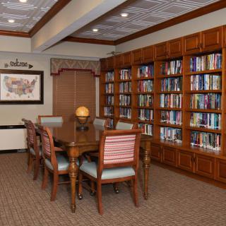 A cozy library room with a wooden table, chairs, and bookshelves filled with books.