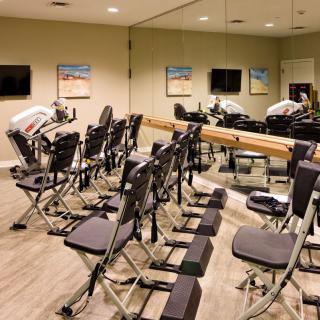 A gym room equipped with exercise machines and chairs, featuring mirrored walls.