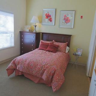 A cozy bedroom featuring a bed with pink bedding, wooden furniture, and floral artwork on the walls.