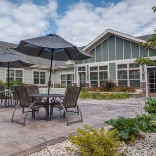 A cozy patio area with tables, chairs, and umbrellas in a garden setting beside a house.