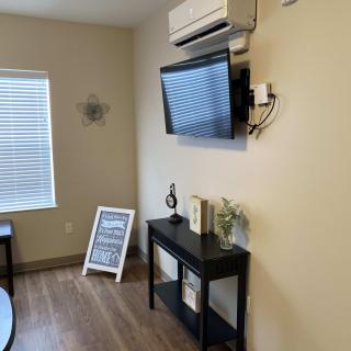A cozy living room corner with a mounted TV and air conditioner, decorated with a small table, books, and plants.