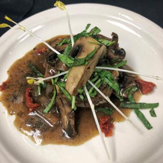 A gourmet dish featuring mushrooms and greens, elegantly arranged with a flavorful sauce on a white plate.