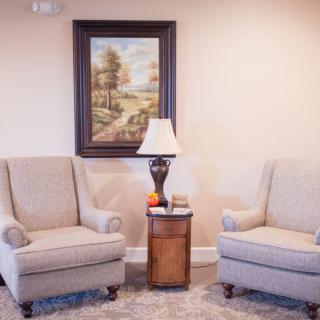 A cozy living room setup with two armchairs, a side table with a lamp, and a landscape painting on the wall.