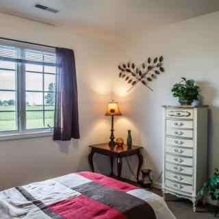 A cozy bedroom with a neatly made bed, a dresser, and a warm lamp on a side table near the window.