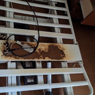 A damaged bed frame with visible rust and an electrical cord on top.