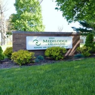 A building sign for The Medilodge of Kalamazoo surrounded by lush greenery and trees.