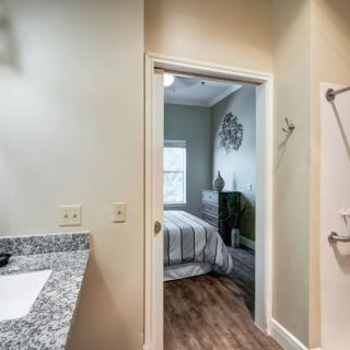 View of a bedroom through a bathroom doorway, featuring modern decor and wooden flooring.