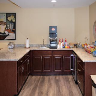 A modern office pantry with a coffee machine, various snacks, and beverages on the counter.