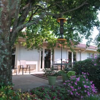 A serene garden view featuring a house with a patio surrounded by lush greenery and colorful flowers.