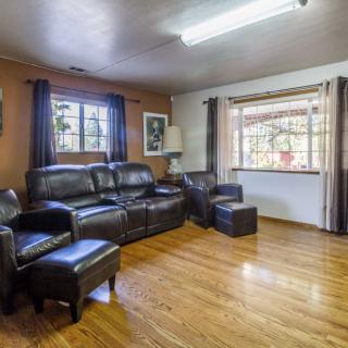 A cozy living room with leather seating and hardwood floors, illuminated by natural light from large windows.