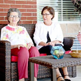 Two women sitting on wicker chairs outside, engaged in conversation.