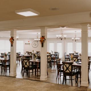 An empty dining room with neatly arranged tables and chairs, featuring decorative columns.