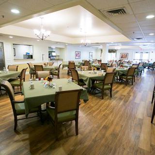 A spacious dining room with tables and chairs, featuring a wooden floor and a chandelier.