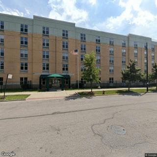 A multi-story residential apartment building with trees lining the street on a clear day.