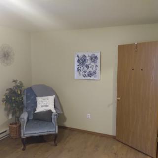 A cozy room corner with a chair, decorative plant, and floral artwork on the wall.