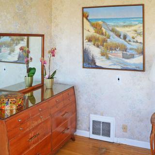 A cozy bedroom corner featuring a wooden dresser with a mirror and decorative items, alongside a landscape painting on the wall.