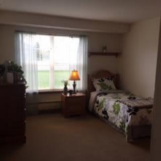 A cozy bedroom with a single bed, dresser, and a lamp near the window.