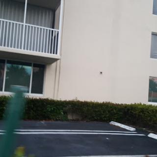 A view of a residential building featuring a balcony and adjacent parking area.