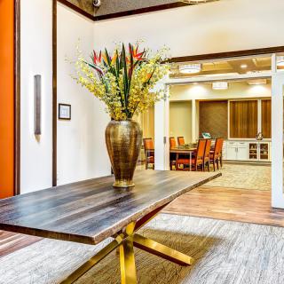 A modern interior space featuring a wooden table with a vase of flowers, leading into a conference room.