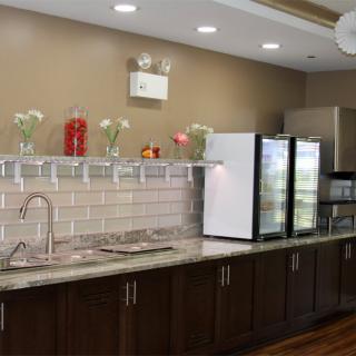 A modern kitchen area with dark wood cabinets, a sink, and a refrigerator, adorned with flowers and well-lit.