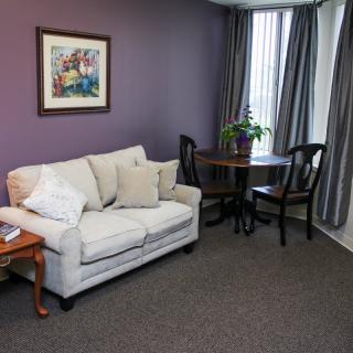 A cozy living room with a sofa, table, chairs, and a colorful painting on the wall.