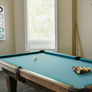 A pool table set up in a game room with cue sticks resting against the wall.