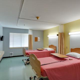 A well-lit hospital patient room featuring two beds with pink linens.