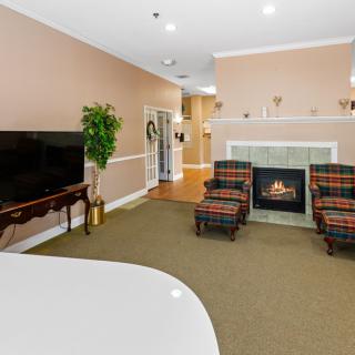 A cozy living room featuring a fireplace, two plaid armchairs, a large television, and tasteful decor.