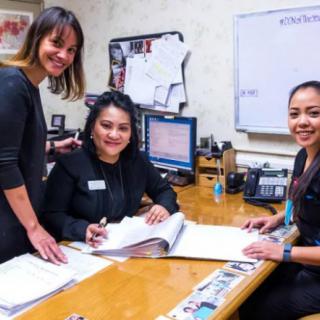 Three women collaborating in an office setting, reviewing documents at a desk.
