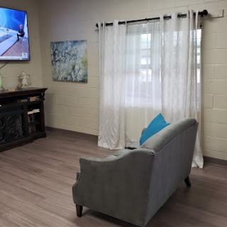 A cozy living room setup featuring a gray sofa, television, and light curtains.