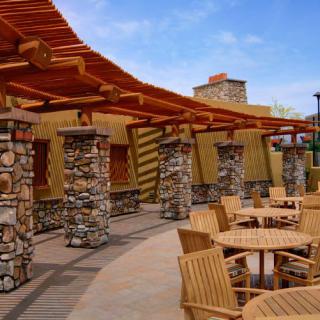 A patio with wooden furniture, stone columns, and a pergola on a sunny day.