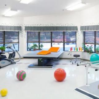 A bright rehabilitation room equipped with a treatment table, exercise machines, and therapy balls.