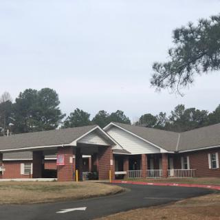 A single-story residential building with a welcoming entrance, surrounded by trees under a cloudy sky.