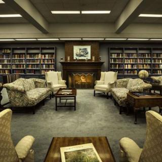 A cozy library reading room with armchairs and a fireplace.