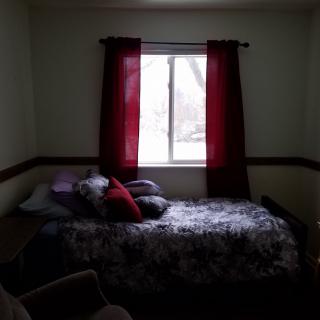 A dimly lit bedroom with a bed under a window featuring red curtains.