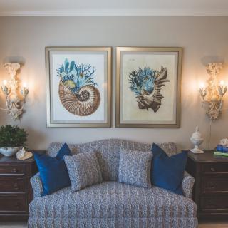 A cozy living room with a patterned couch, blue cushions, and sea-themed artwork above.