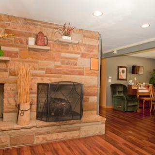 A cozy living room featuring a stone fireplace and wooden floors, seamlessly connecting to the dining area.