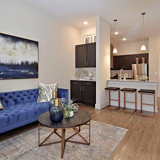 A modern living room with a blue sofa, coffee table, and adjoining kitchen with barstools.