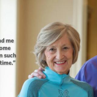 An elderly woman smiling indoors in casual clothing.