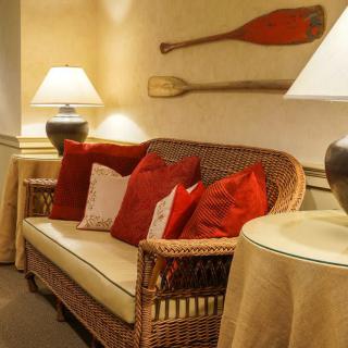 A cozy living room with a wicker sofa adorned with red and white cushions, illuminated by stylish lamps and decorated with paddles on the wall.