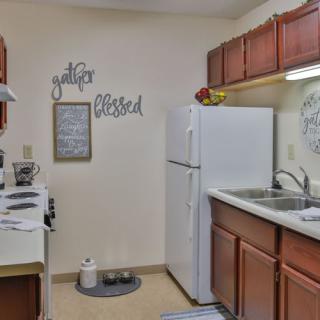 A cozy kitchen with wooden cabinets, a white refrigerator, and stove, featuring wall decor with inspirational words.