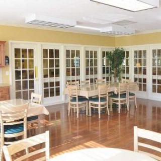 A bright dining area with wooden tables and chairs, featuring large windows and a polished wooden floor.