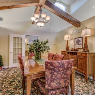 A cozy dining room featuring a wooden table with floral-patterned chairs, illuminated by a chandelier and complemented by decorative lamps and plants.