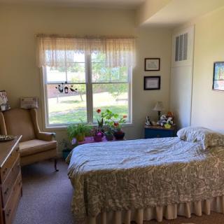 A cozy bedroom featuring a neatly made bed, comfortable chair, and bright natural light coming through the window.