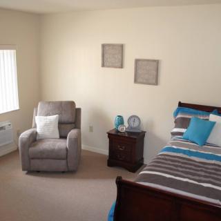 A cozy bedroom with a bed, armchair, and nightstand, featuring neutral tones and colorful accents.