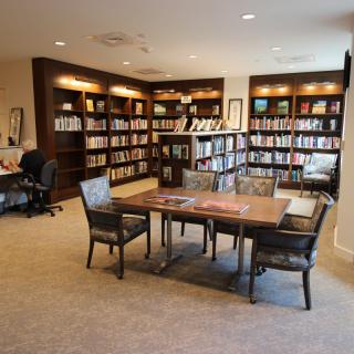 A cozy library with bookshelves, a central table, and chairs for reading.