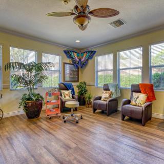 A cozy living room setting with comfortable chairs, large windows, and lush indoor plants.